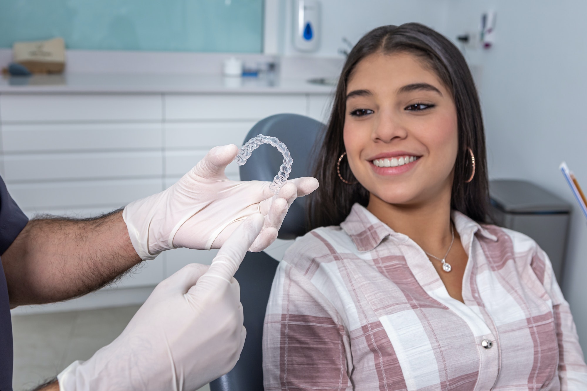 Unrecognizable dentist showing silicone aligners to positive ethnic girl